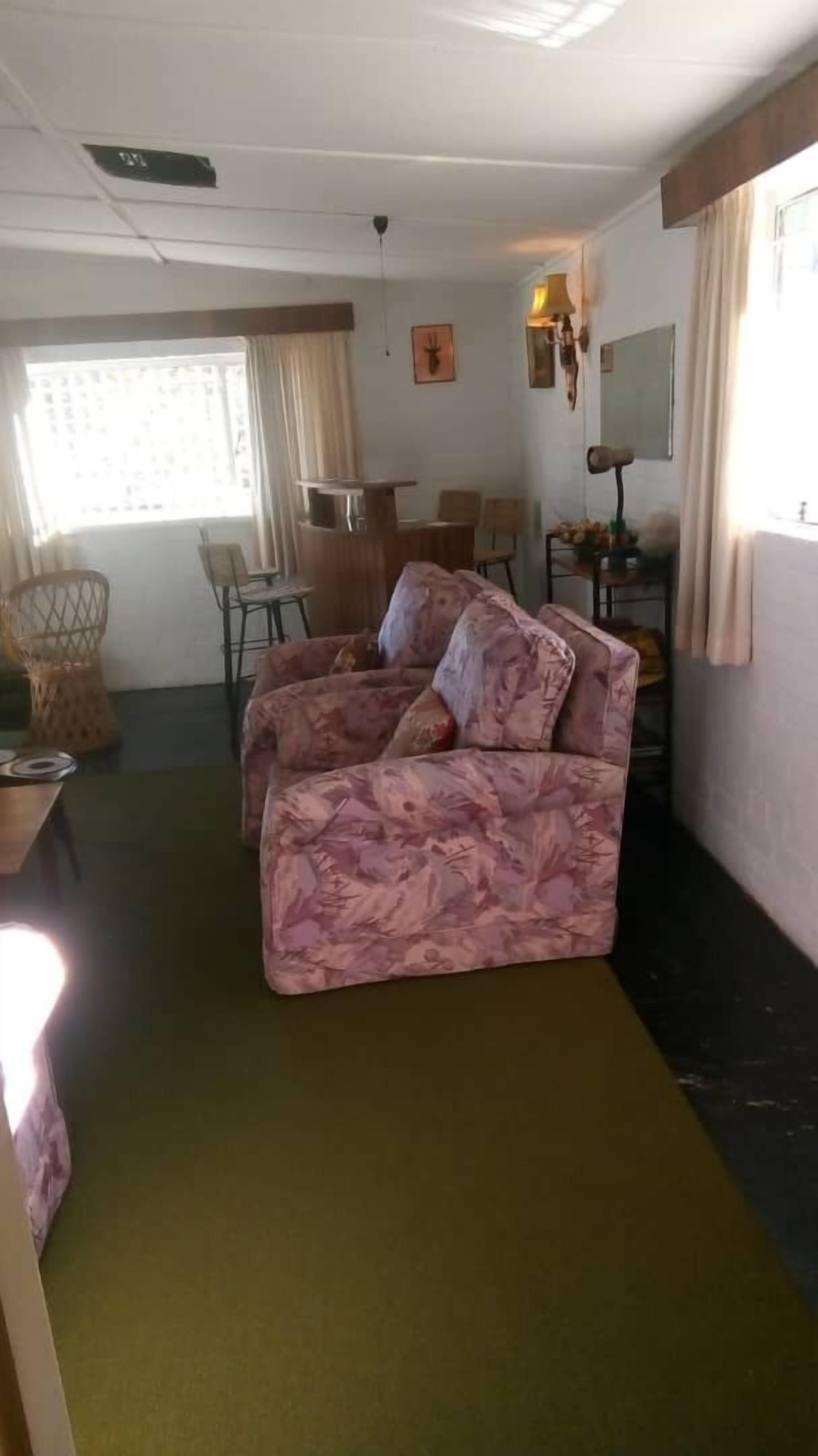 Una habitación con un sofá estampado con motivos florales, una mesa de comedor con sillas, una pequeña cocina y un ventanal con cortinas.
