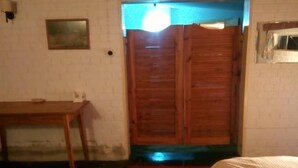 Ein Zimmer mit Holztür, einem Bett mit weißer Bettdecke, einem kleinen Tisch und einem roten Teppich.