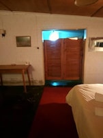 Una habitación con puerta de madera, una cama con cubrecama blanco, una mesita y una alfombra roja.