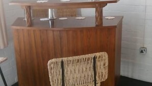 Eine Bar mit einer Holztresen, einem gewebten Stuhl und einer Wandleuchte.