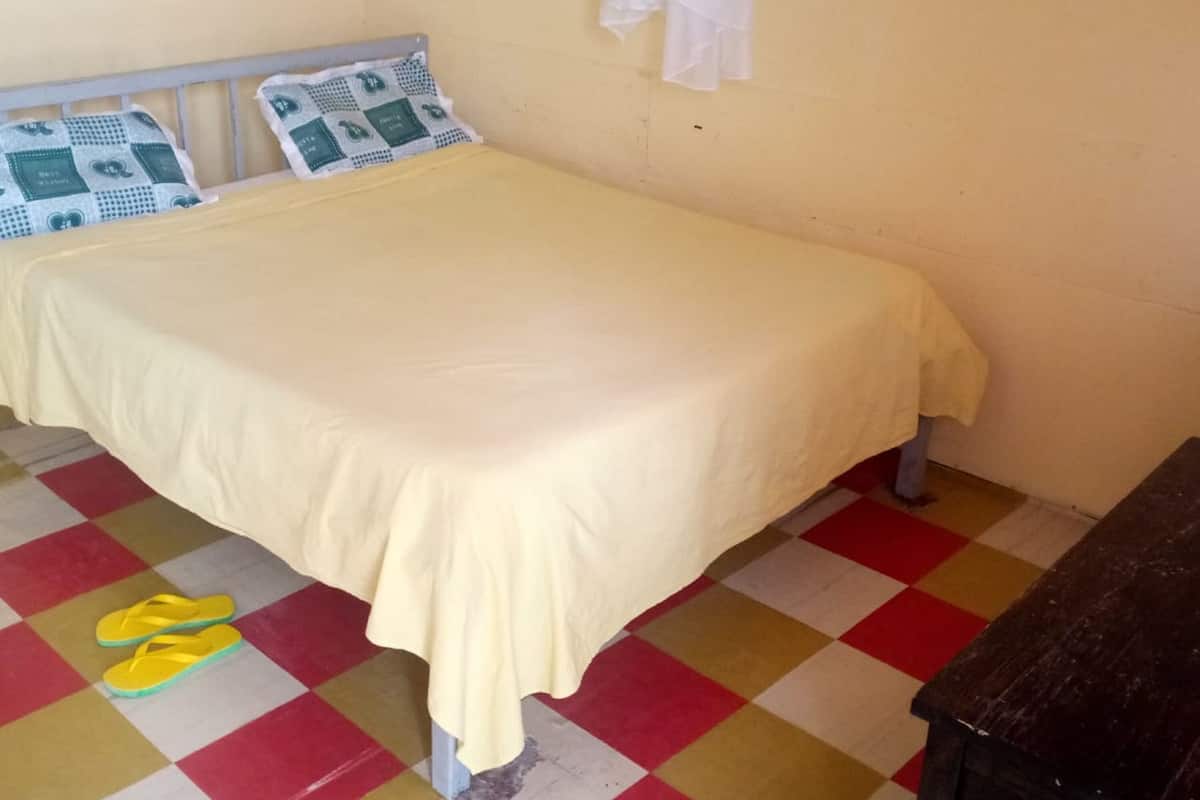A single bed with a yellow bedspread, a checkered floor, and a wooden table.