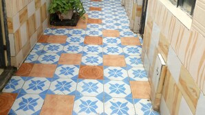 Un pasillo estrecho con baldosas azules y anaranjadas decorativas en el suelo, una planta en maceta y una ventana a la derecha.