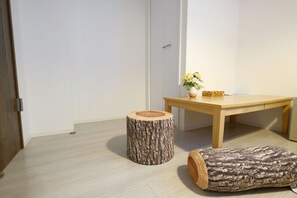 A room with a wooden table, a round wooden stool, and a small table with a vase of flowers.