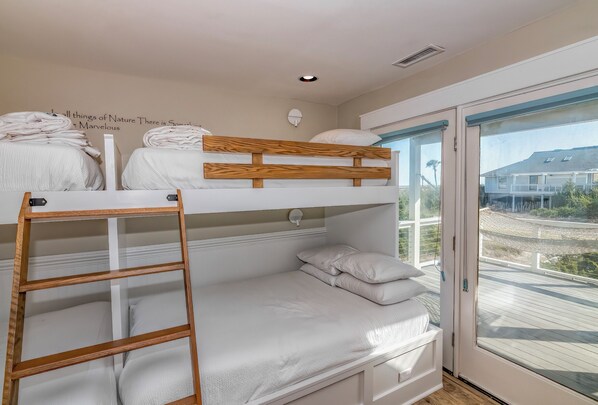 Habitación con literas, una escalera de madera, un colchón blanco y vistas a un balcón.