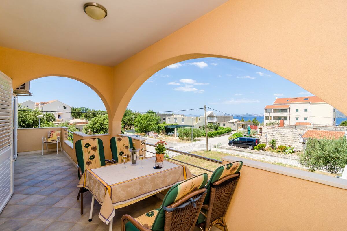 Un balcon avec une table et des chaises, une vue sur la mer et un ciel dégagé.