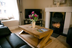 Ein modernes Wohnzimmer mit Couchtisch aus Holz, einer schwarzen Ledersofa, einem Flachbildfernseher und einem Kamin.
