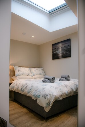A bedroom with a skylight, a bed with floral bedding, and a painting of a sunset.