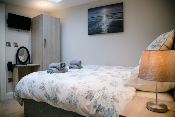 A bedroom with a bed, a nightstand, a lamp, a TV mounted on the wall, and a painting of a seascape.