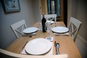 Ein Esszimmer mit einem Tisch, der mit weißen Tellern, Besteck und Weingläsern gedeckt ist, mit einer Weinflasche und einem gerahmten Bild an der Wand.