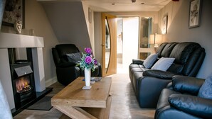 A modern living room with a fireplace, leather sofas, and a wooden coffee table. - Eske Holiday Apartment (Donegal Town)
