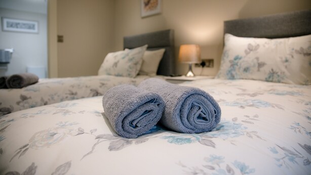 A neatly made bed with floral bedding and a rolled towel. - Eske Holiday Apartment (Donegal Town)