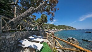 Une terrasse en bord de mer, avec des murs en pierre, des fauteuils blancs et une vue sur la mer.