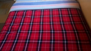 A bed with a red plaid bedspread and a quilt with floral patterns. - Top Lodge (Naivasha)