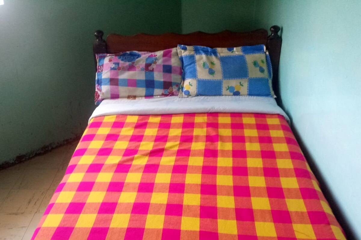 A bed with a checkered bedspread in red, yellow, and pink.