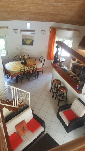 Un comedor con una mesa redonda y sillas, una cocina con mostrador y taburetes, y una sala de estar con sofá y cojines.