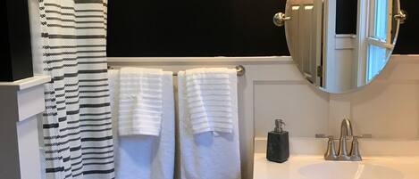 A bathroom with a black wall, a white sink, a round mirror, and two towels hanging on the wall.
