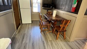 A compact kitchen with a wooden dining table and chairs, a white refrigerator, a microwave, and a fire extinguisher on the wall.