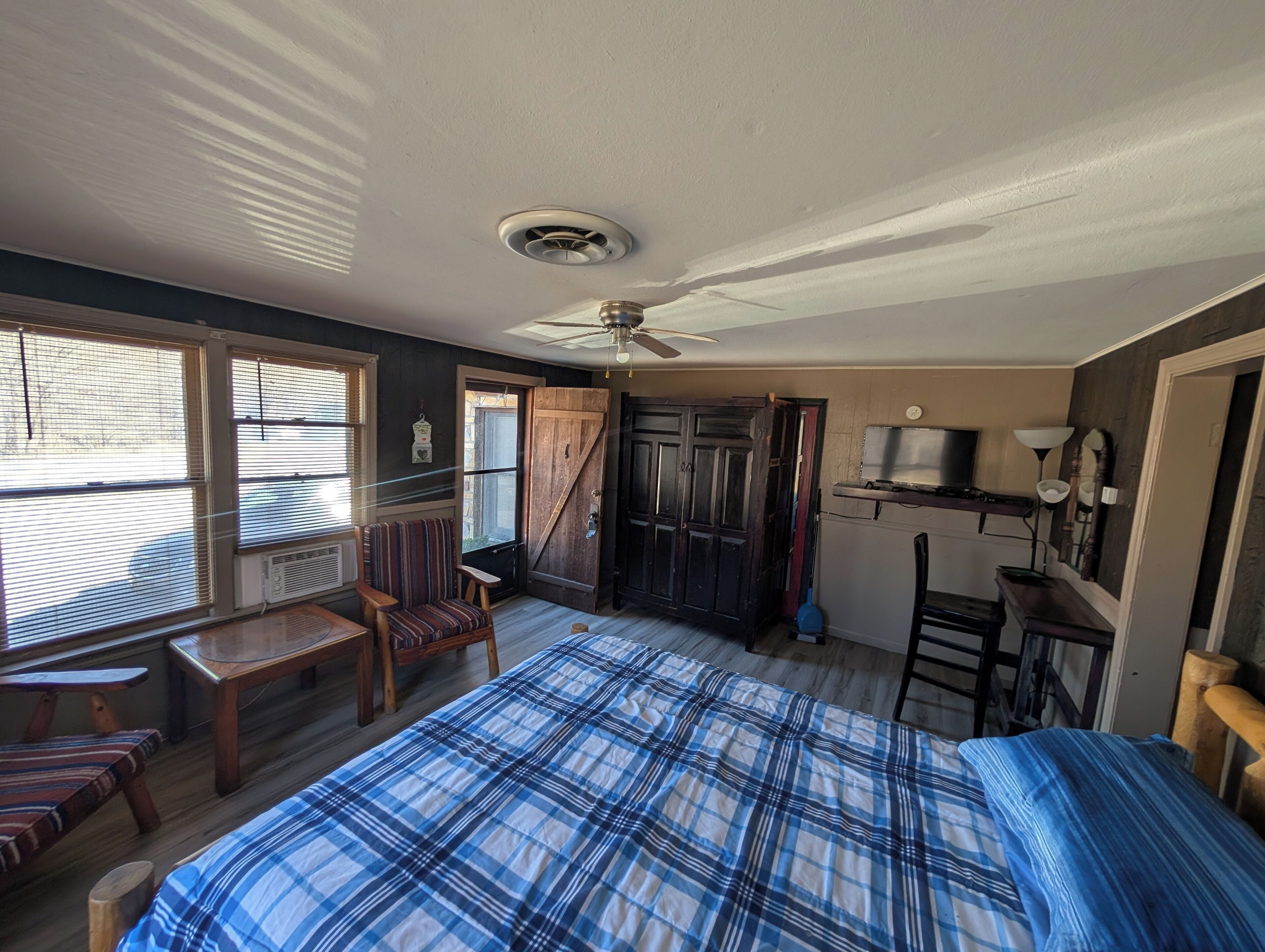A bedroom with a bed, a chair, a desk, a ceiling fan, and a window with blinds.