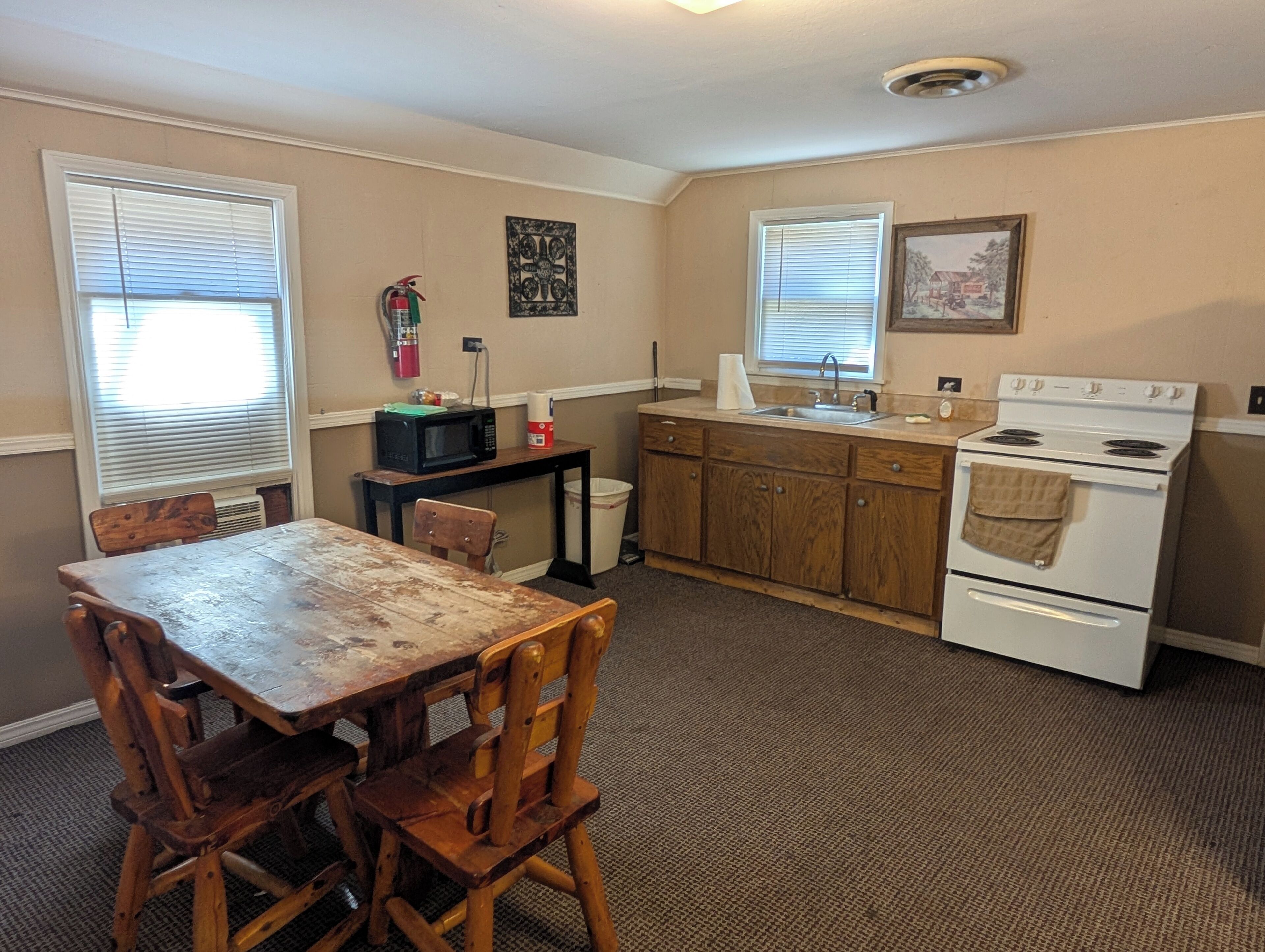 Une cuisine compacte avec une table et des chaises en bois, une cuisinière, un évier et un four à micro-ondes posé sur une petite table.