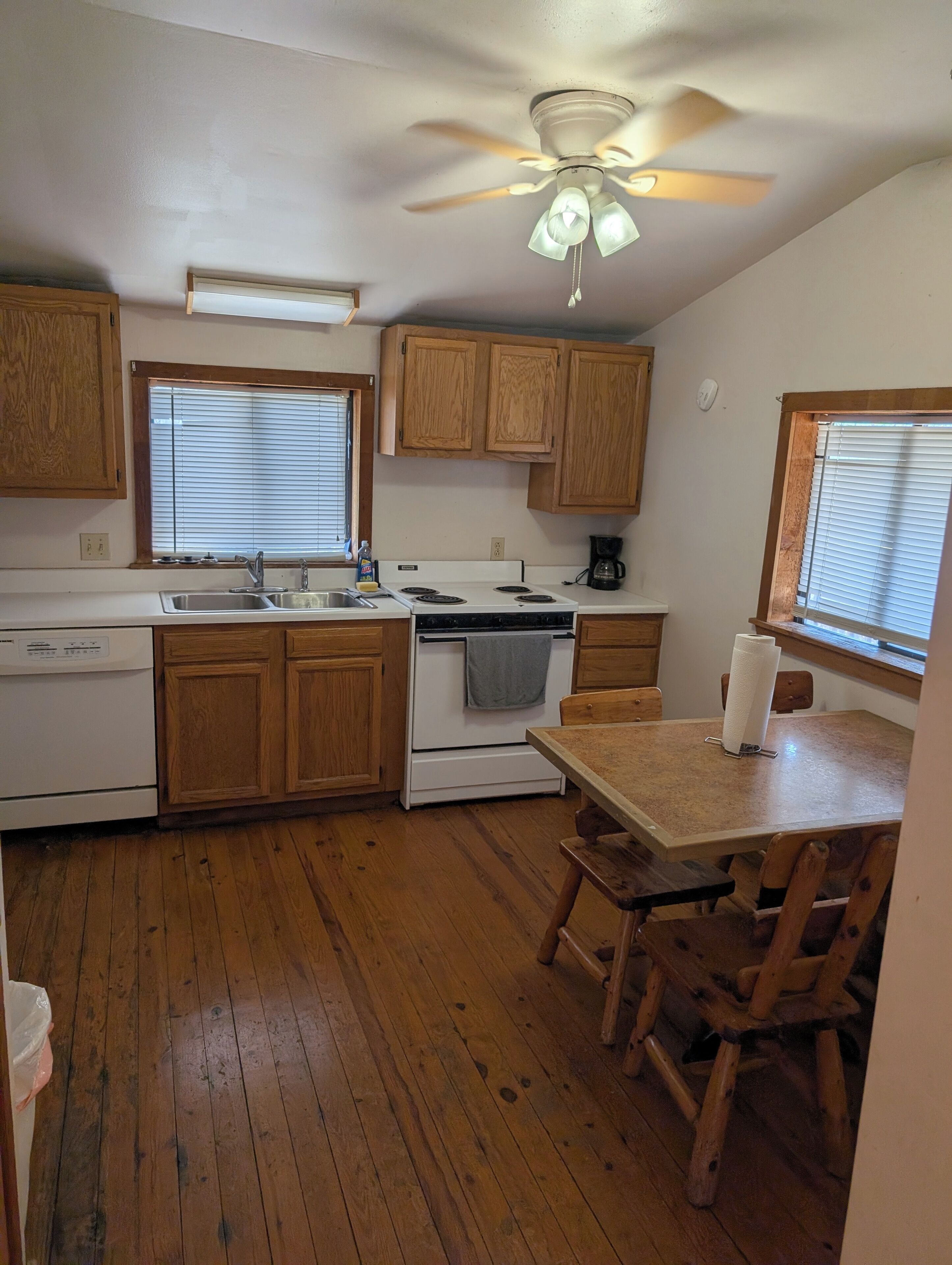 A kitchen with wooden cabinets, a stove, a sink, and a ceiling fan.