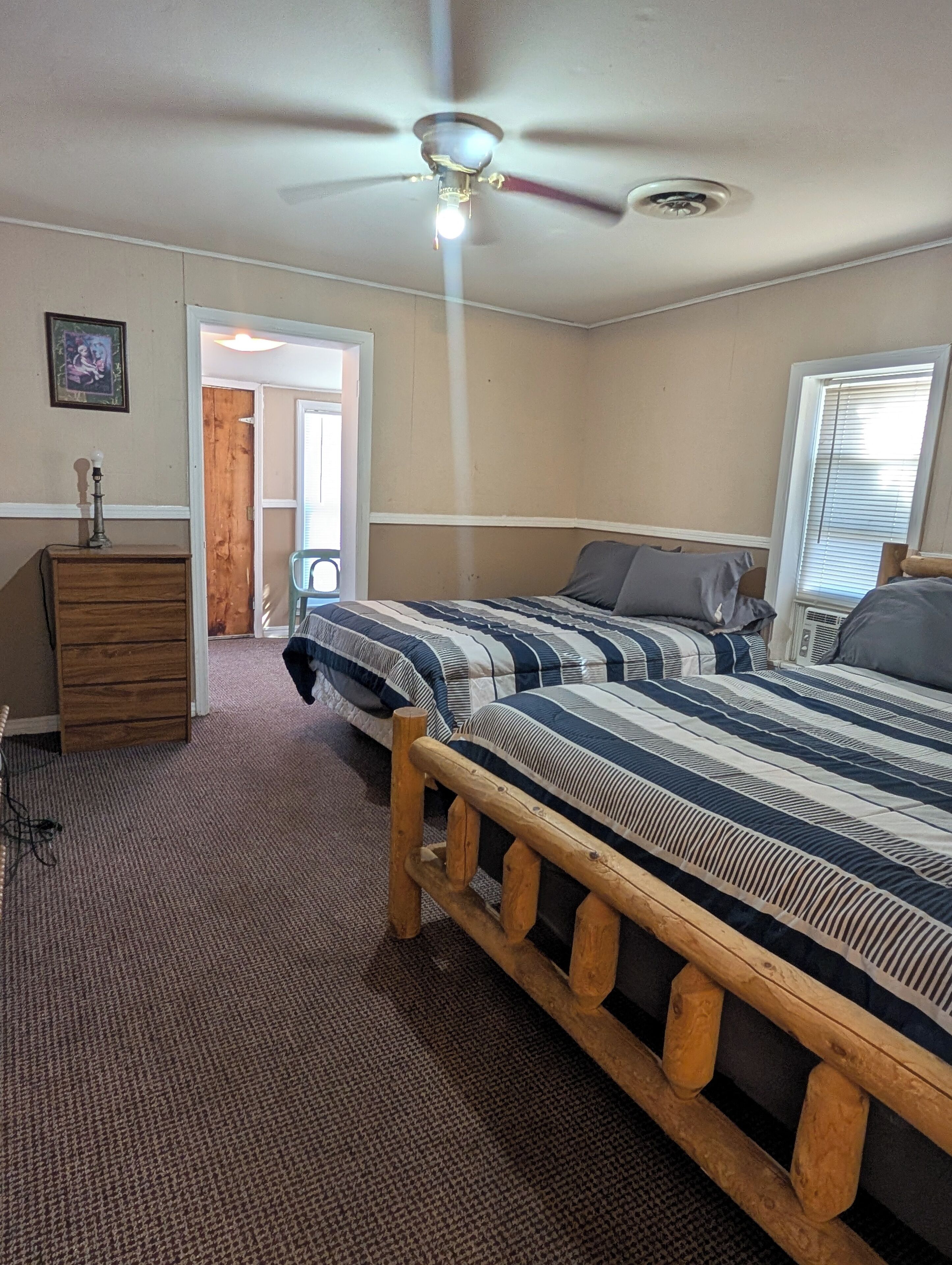 A bedroom with a wooden bed frame, a ceiling fan, a dresser, and a door leading to another room.