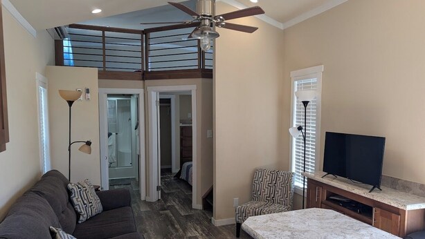 A modern living room with a sofa, a coffee table, a TV, and a ceiling fan. - Cedarvale Cabins at Turner Falls (Davis)