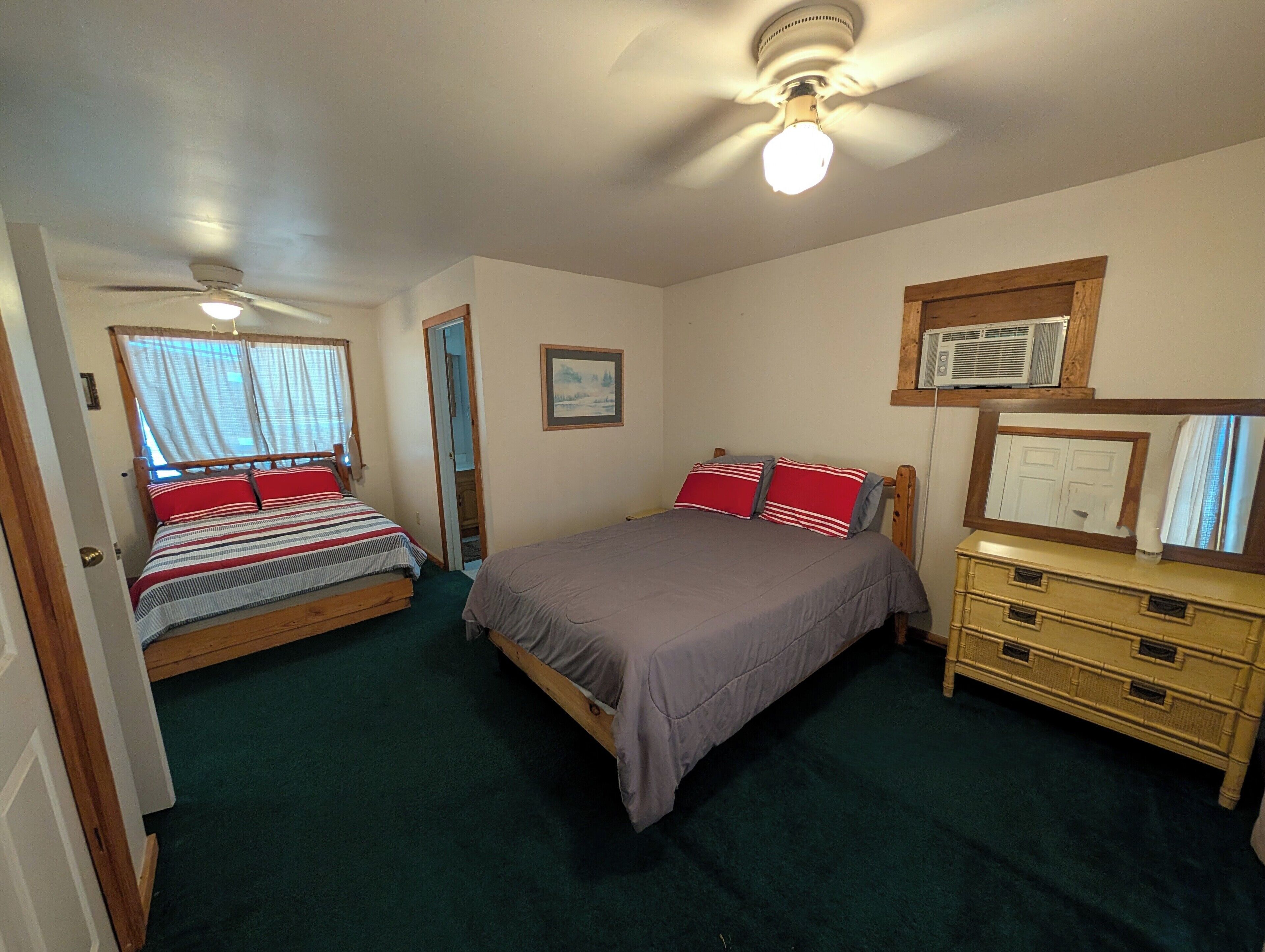 A bedroom with two beds, a ceiling fan, a dresser, and a window with curtains.