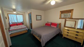 A bedroom with two beds, a ceiling fan, a dresser, and a window with curtains.