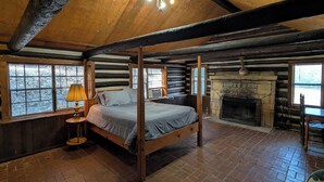 A log cabin bedroom with a four-poster bed, a stone fireplace, and large windows. - Cedarvale Cabins at Turner Falls (Davis)
