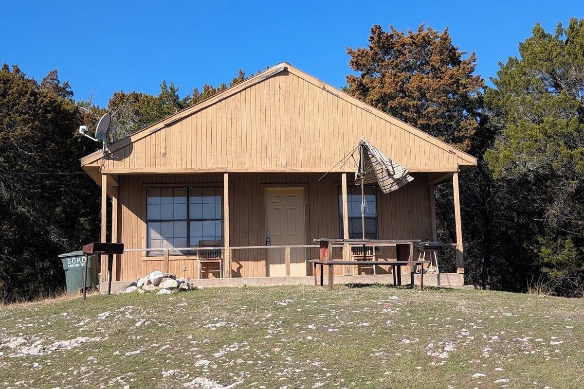 A wooden cabin with a porch, large windows, and a picnic table.