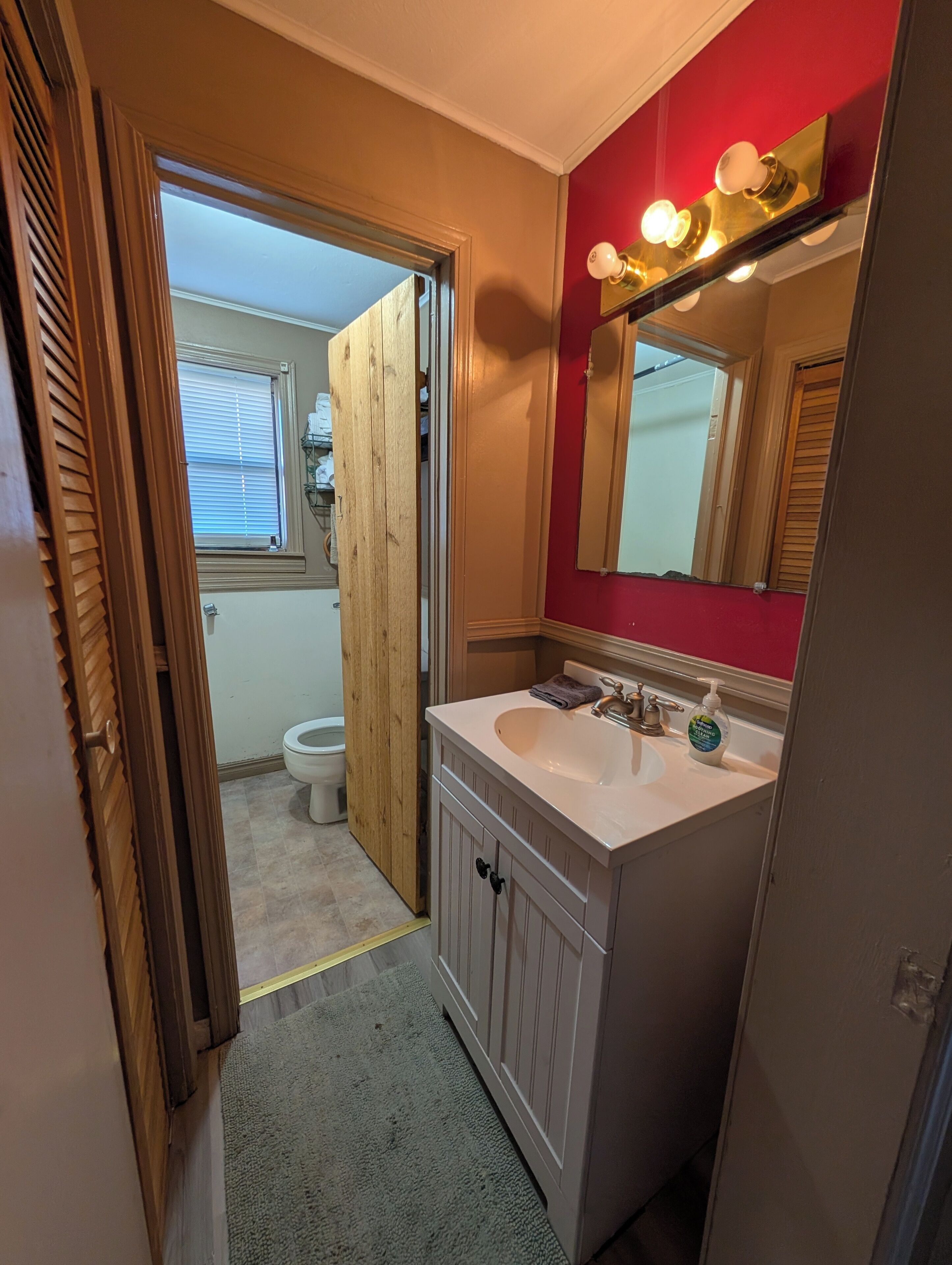 A bathroom with a white sink, a mirror with lights, and a wooden door.