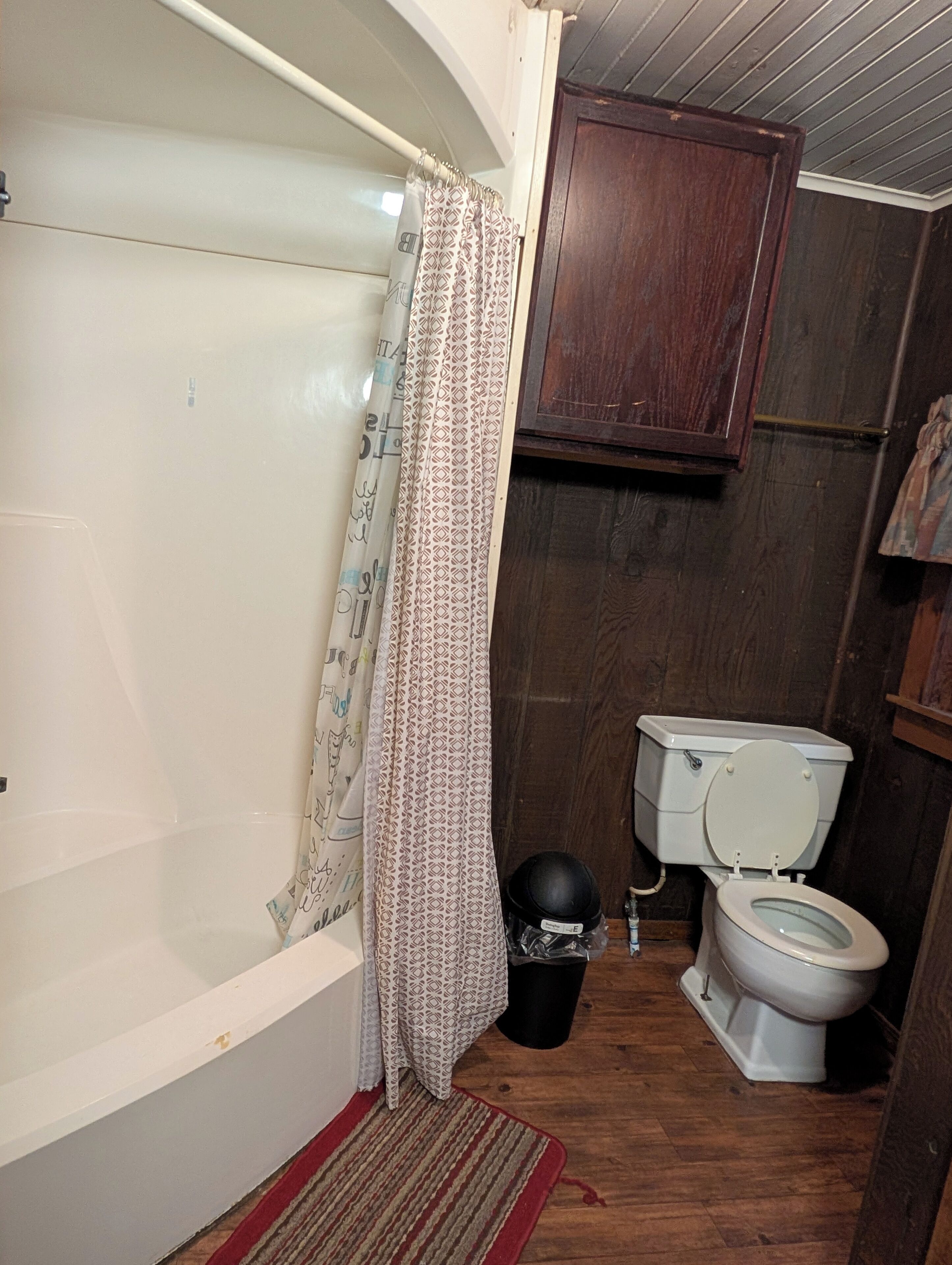 A small bathroom with a bathtub, toilet, and a wooden cabinet.