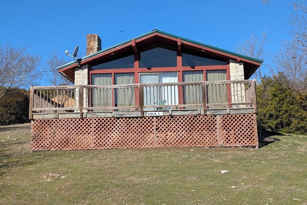 A cabin with a wooden deck, a stone chimney, and a sign indicating it is cabin number 5.