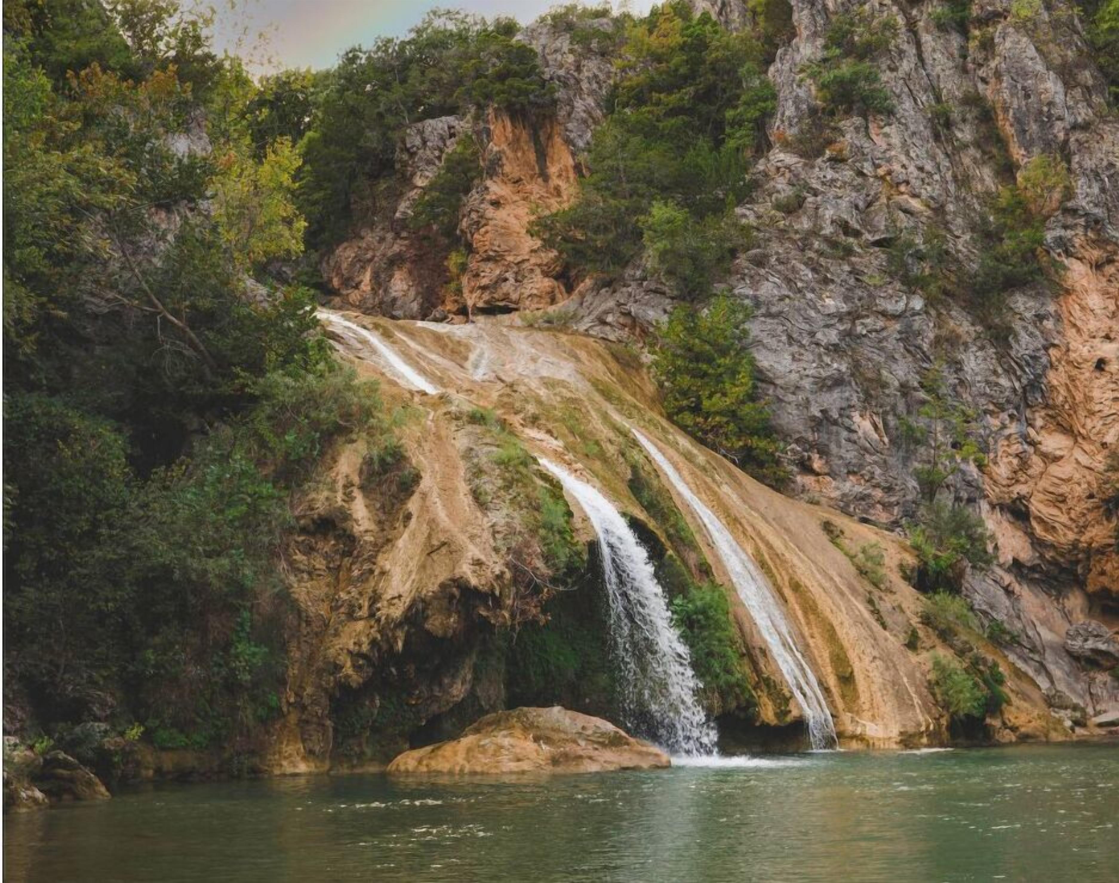 A waterfall cascading down a rocky cliff into a body of water, surrounded by dense greenery.