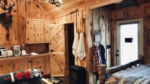 Ein rustikales Cabin-Interieur mit Holzwänden, Kamin, einem Bett und einer Küchenzeile mit Kaffeemaschine und Toaster.