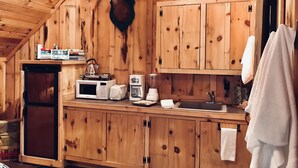 Eine rustikale Holzhüttenküche mit aufgehängtem Hirschkopf, Holzschränken, einem Kühlschrank, einer Mikrowelle, einem Wasserkocher und einer Kaffeemaschine.