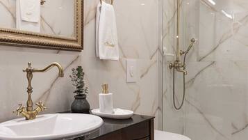 Une salle de bain avec un lavabo en marbre, des robinets dorés, une douche en verre et des toilettes.