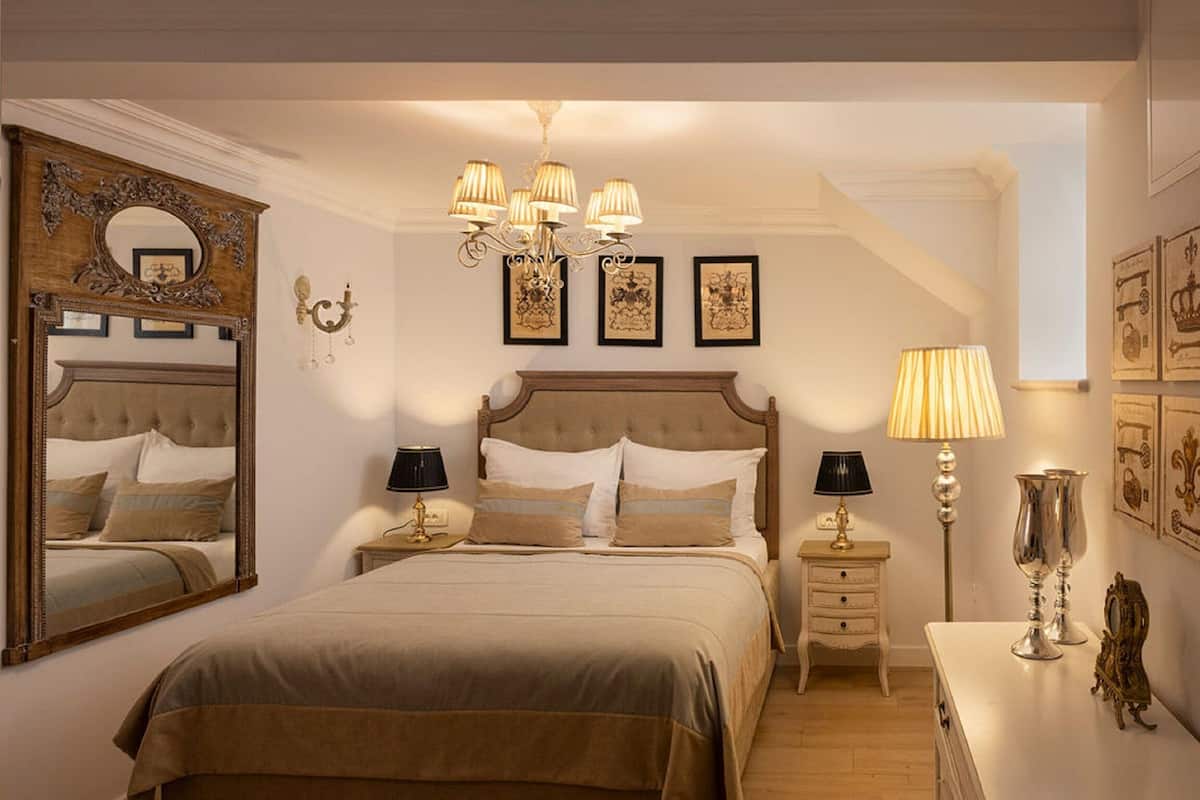 A bedroom with a large bed, two bedside tables, a chandelier, and framed artwork on the walls.