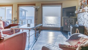 A spacious living area with a large glass door leading to a balcony, a television, and a fireplace. - Oceanfront Whale Watching Retreat (Depoe Bay)