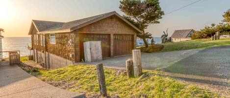 A coastal house with a garage, a grassy yard, and a view of the sea.