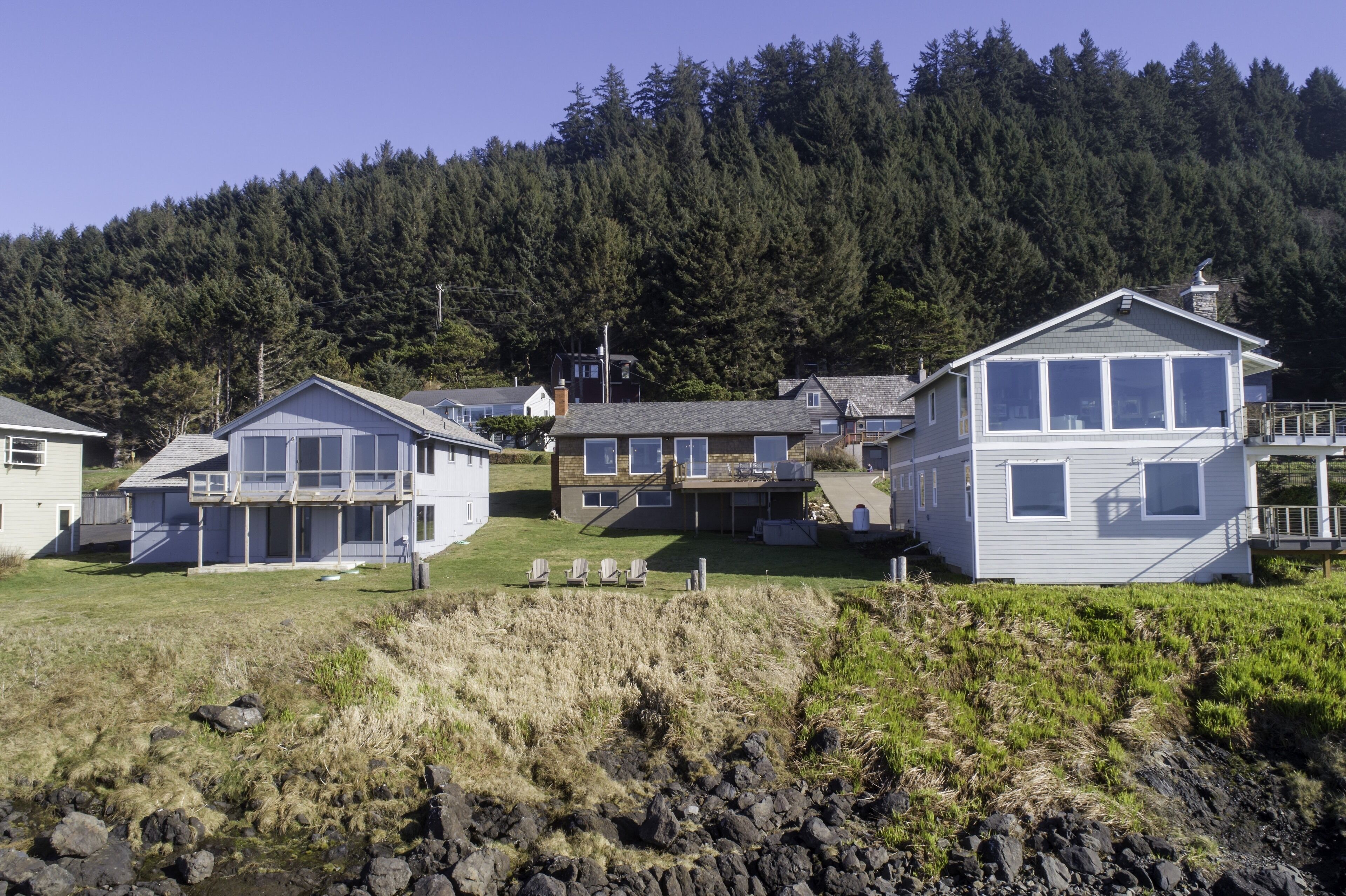 A coastal residential area with houses featuring large windows and a grassy yard.