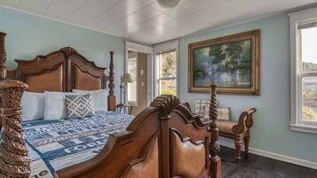 A bedroom with a large bed, a wooden chair, a painting on the wall, and a view through the window.
