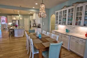 Uma cozinha com mesa de jantar de madeira, cadeiras brancas e um candelabro.