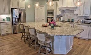 Uma cozinha com ilha central, banquetas, eletrodomésticos de aço inoxidável e iluminação pendente.