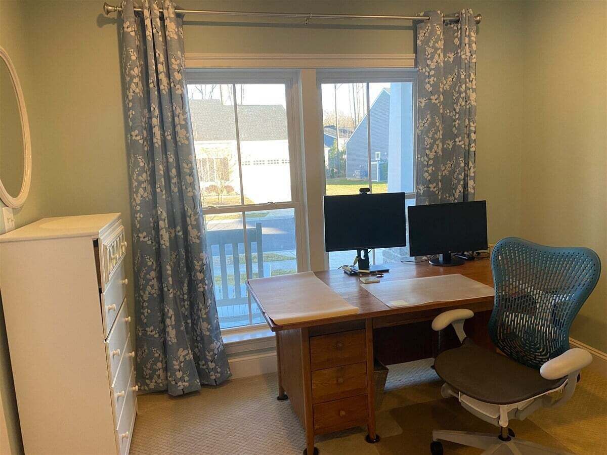 A room with a desk, two monitors, a chair, a dresser, and a window with curtains.