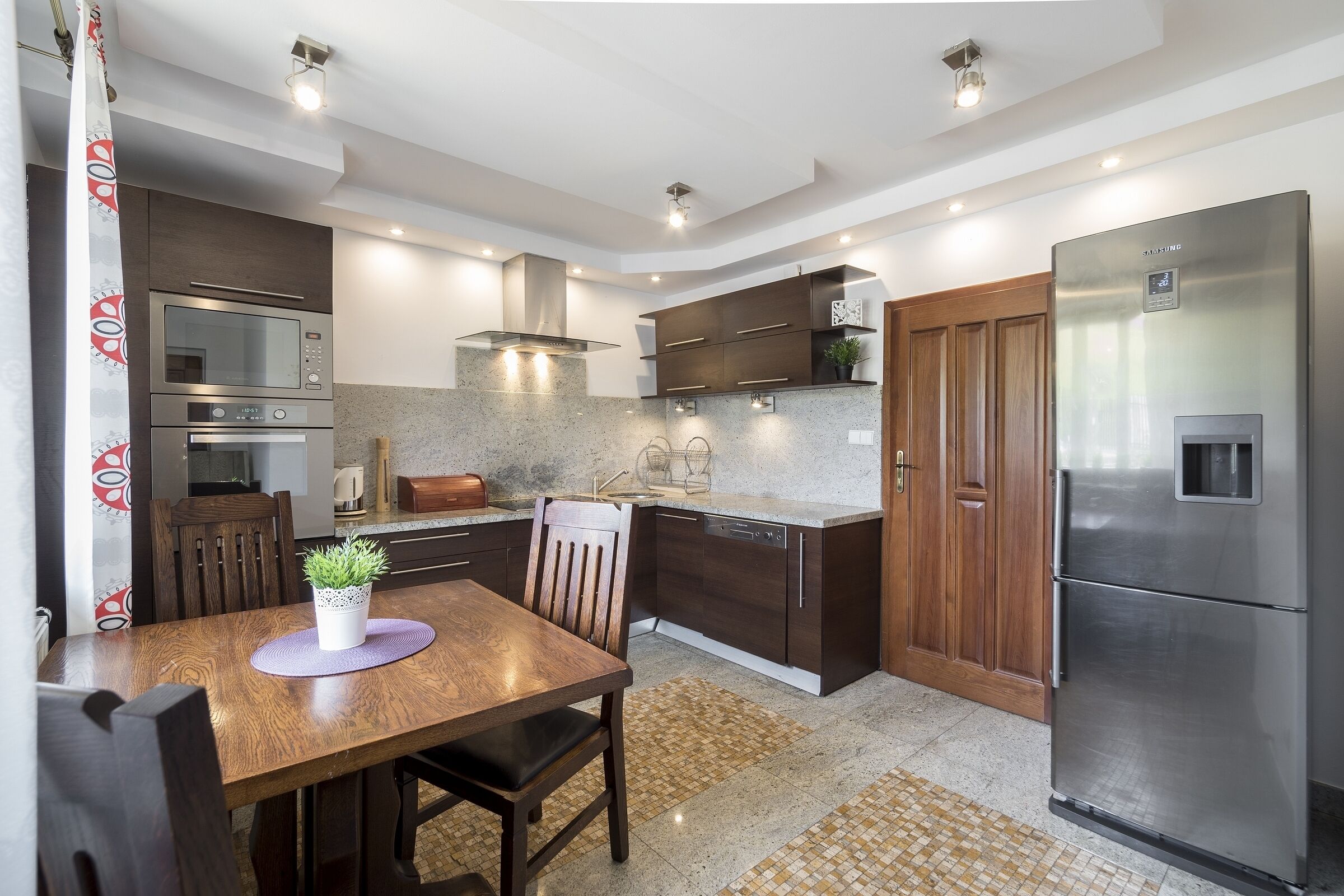 Moderni keittiö, jossa on integroidut kodinkoneet, puukaapit sekä ruokailutila pöytineen ja tuoleineen.