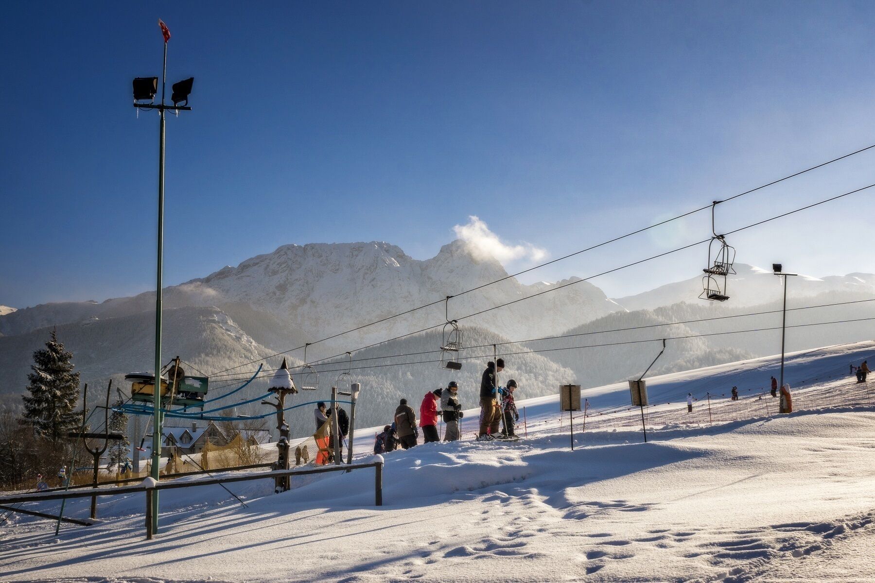 Eine Skipiste mit Sessellift, Skifahrern und einem Berg im Hintergrund.