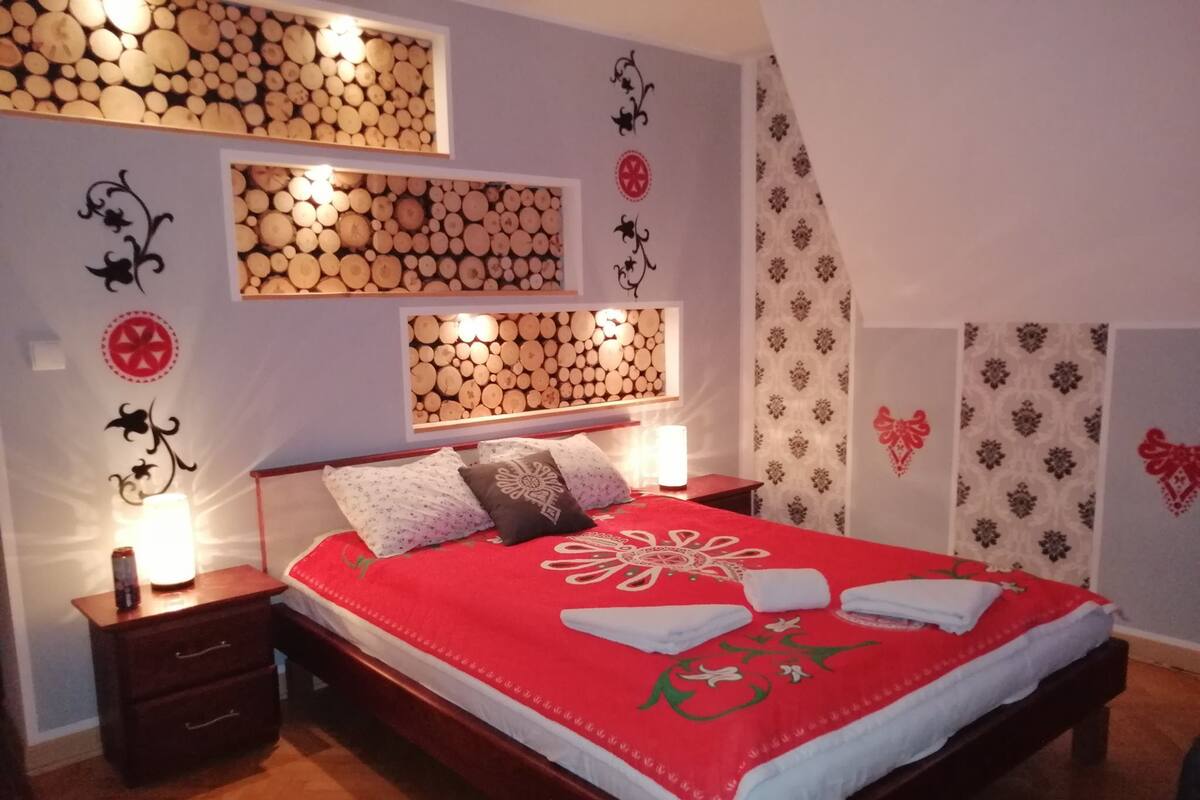 Ein Schlafzimmer mit einem hölzernen Kopfende, einer roten Bettdecke und dekorativen Wandverkleidungen.