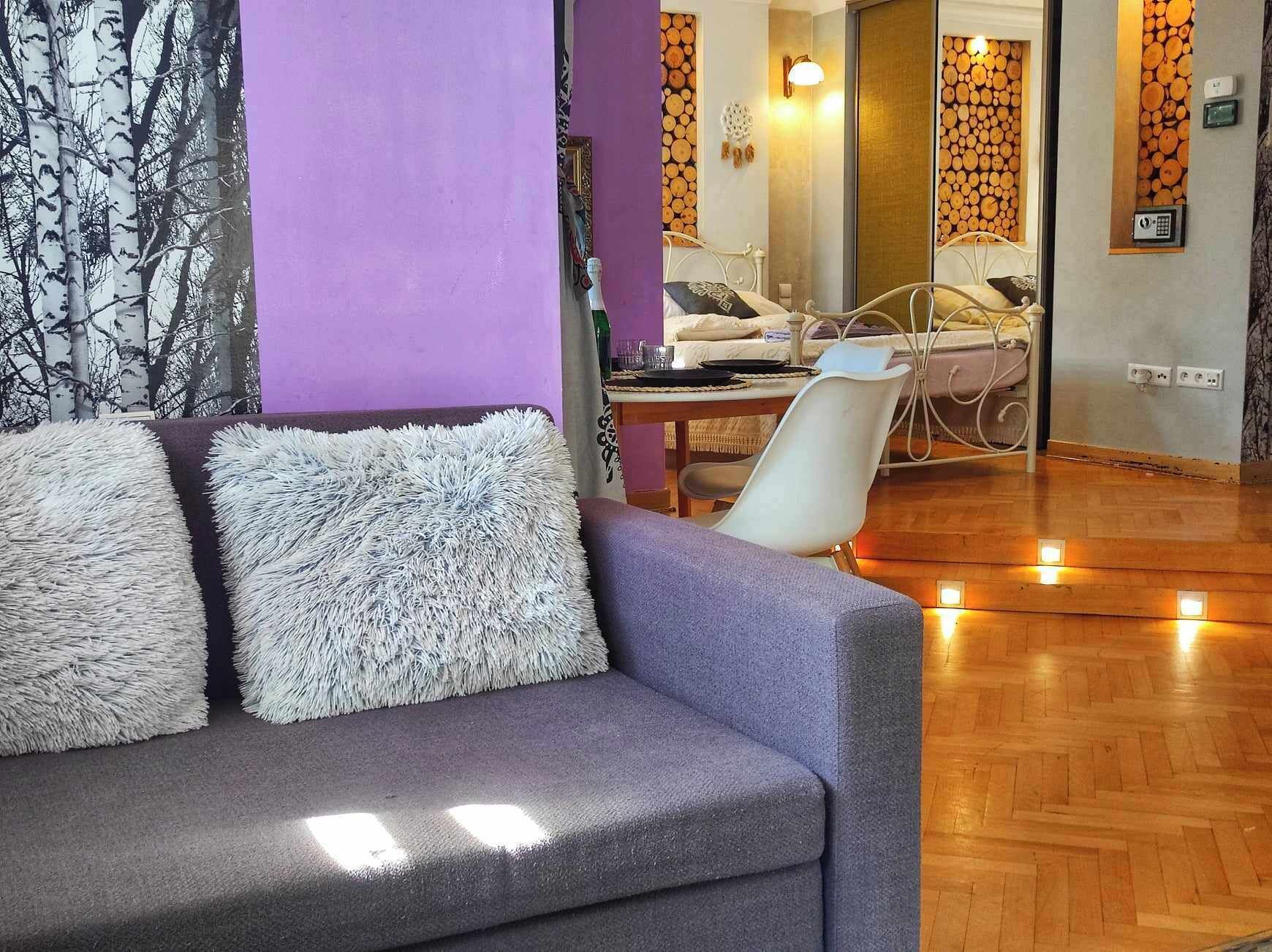 A modern living room with a grey sofa, a dining table, and a mirrored wall.