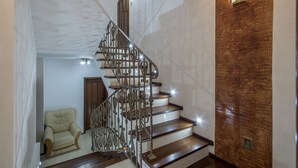 Un escalier orné de rampes en métal ouvragé et de marches en bois, menant à un palier où se trouvent un fauteuil beige et une porte en bois.